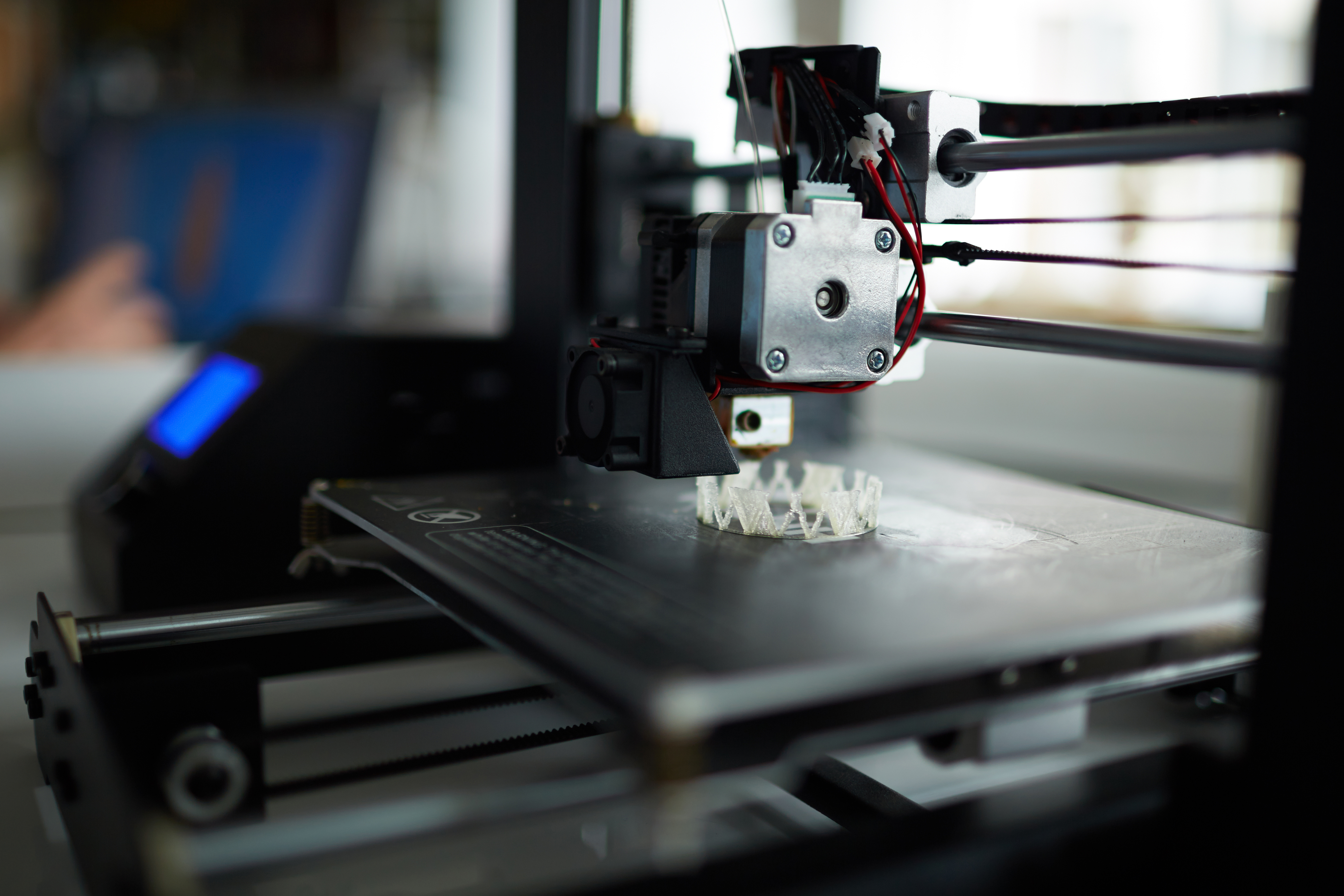 3D printer with extruder head actively printing white plastic object on build platform