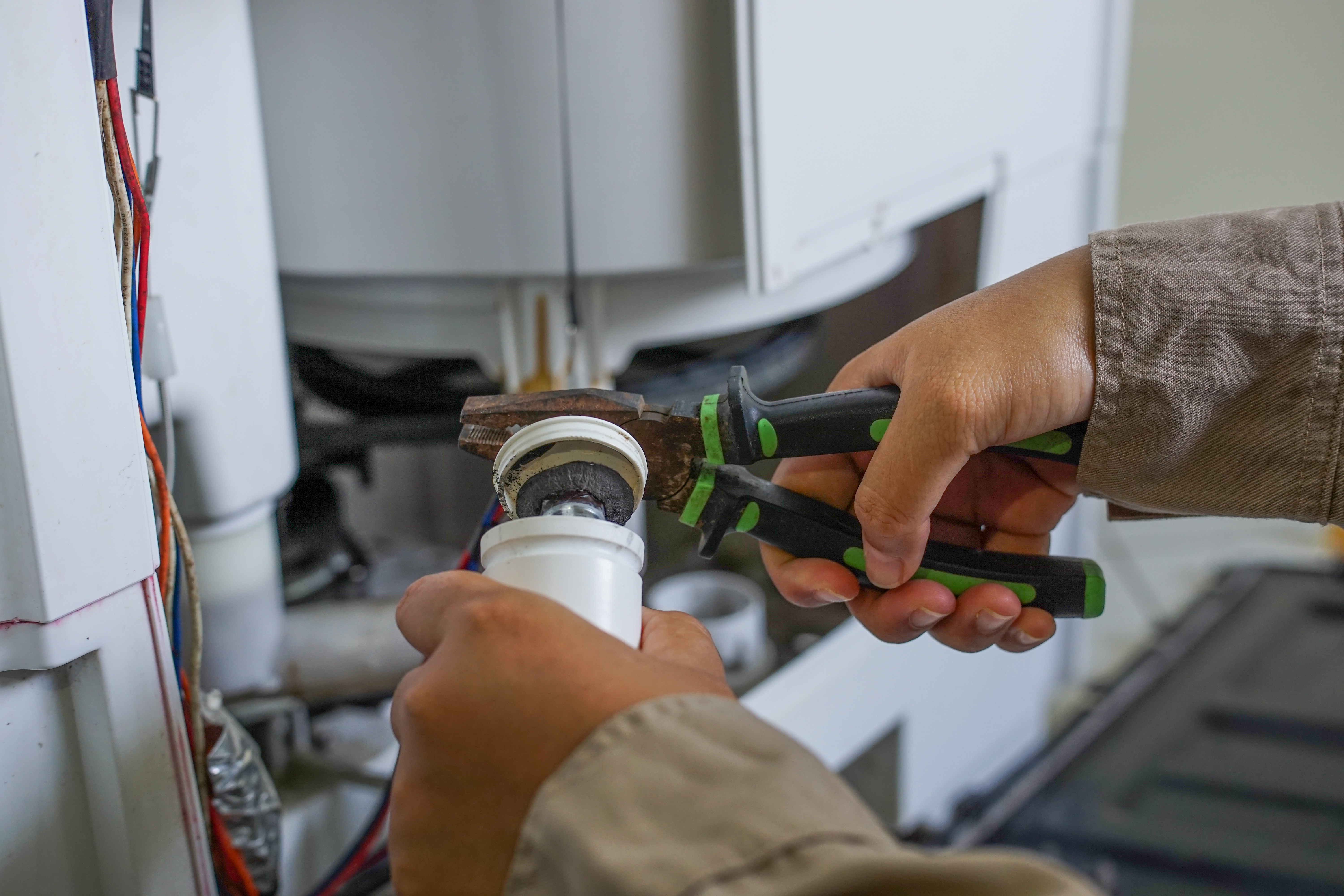 Electrician using pliers to work on a white electrical fixture during installation or repair