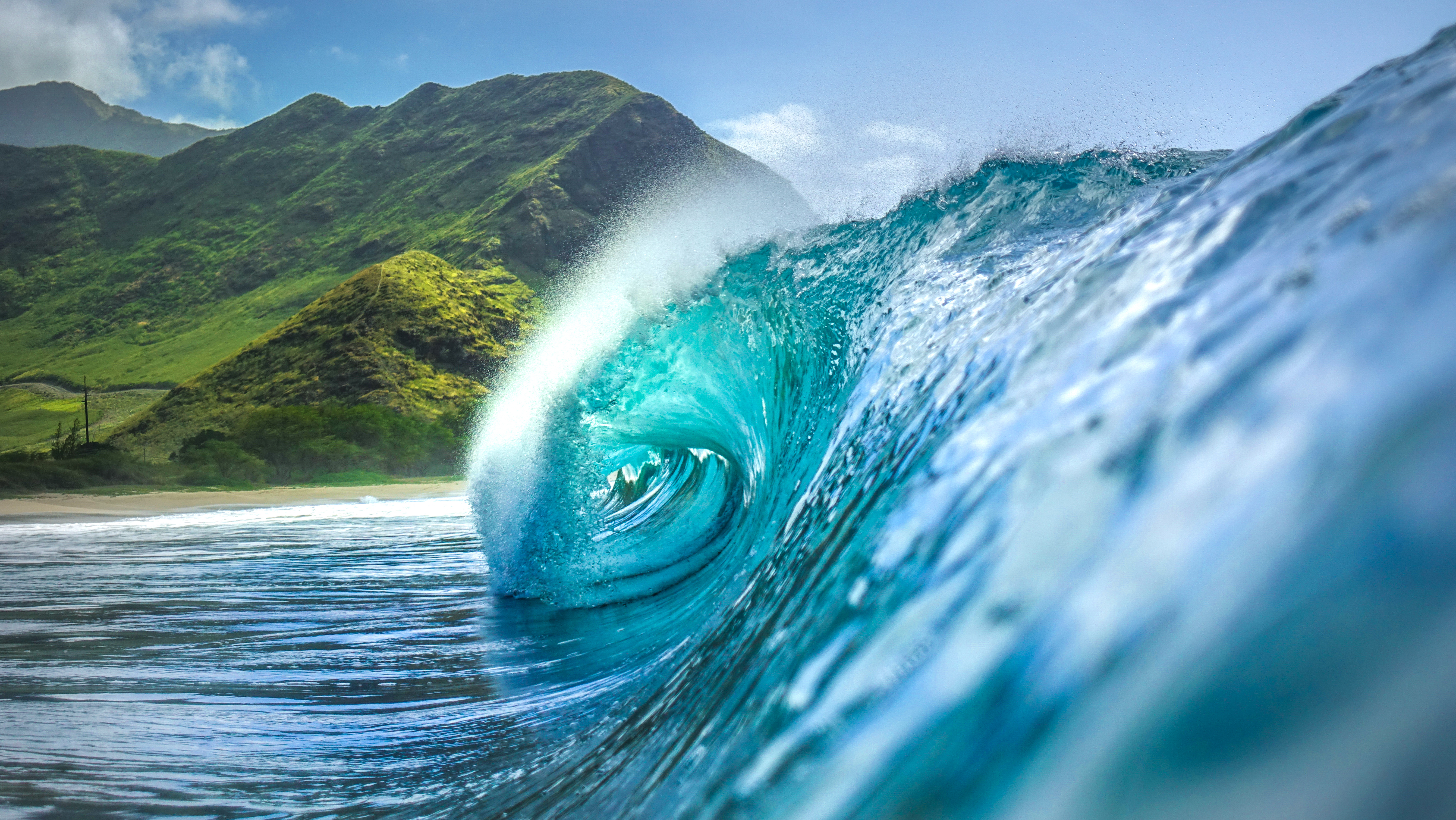 Perfect turquoise wave barrel with tropical green mountains and sandy beach in background